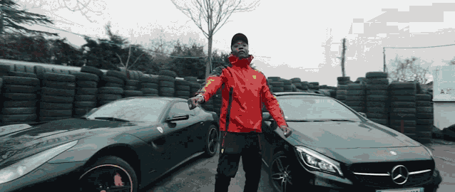 a man in a red jacket stands in front of a stack of tires