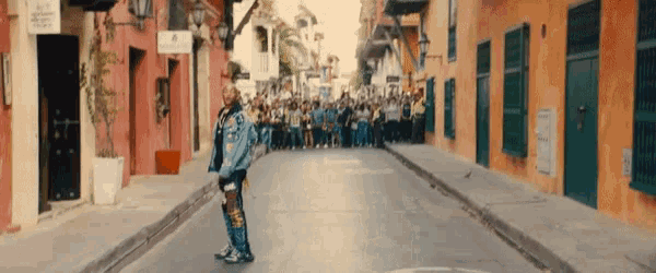 a man in a denim jacket is standing in the middle of a narrow street