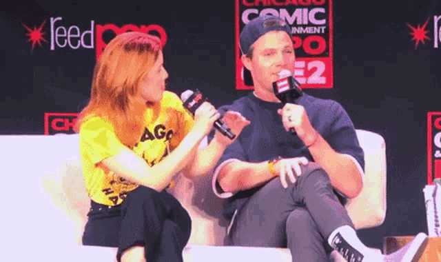 a man and a woman are sitting next to each other on a couch and talking into microphones .