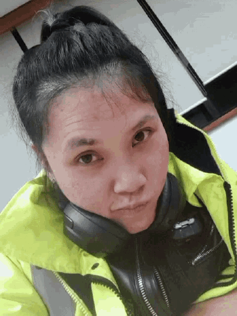 a woman wearing a yellow jacket and black headphones looks at the camera