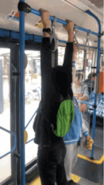 a person with a green backpack is hanging upside down on a blue railing on a bus