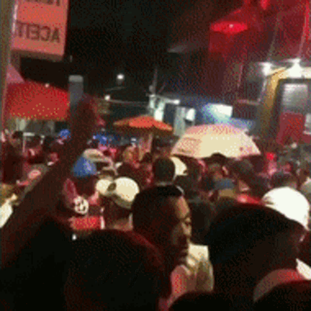 a crowd of people are gathered under an umbrella in front of a sign that says " stella "