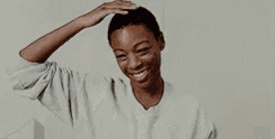 a woman in a grey sweater is smiling and touching her hair .