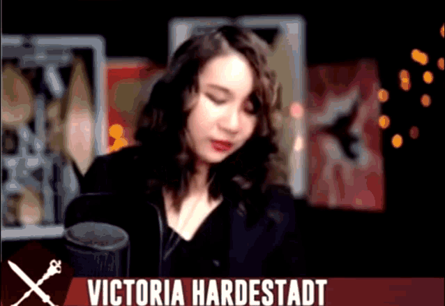a woman stands in front of a microphone with the name victoria hardstadt on the bottom right