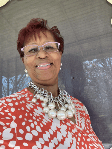 a woman wearing glasses and a pearl necklace smiles at the camera