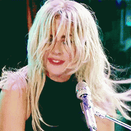 a woman with long blonde hair is singing into a microphone