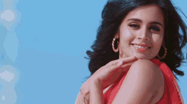 a woman in a red dress and hoop earrings smiles at the camera