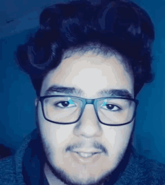 a young man wearing glasses and a beard is smiling for the camera .