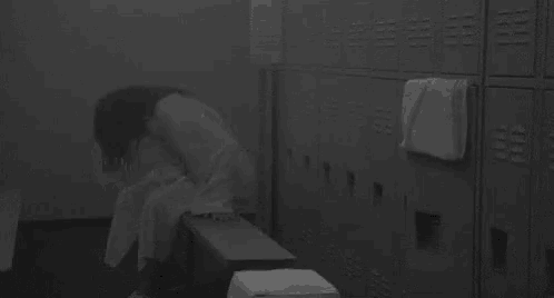 a woman is sitting on a bench in a locker room with a lot of lockers .
