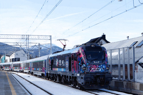 a train with a colorful design on the front of it is going down the tracks