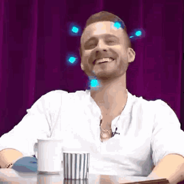 a man is sitting at a table with a cup of coffee and laughing .