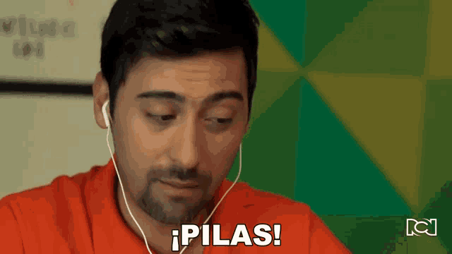 a man wearing headphones says " pilas " in front of a green wall