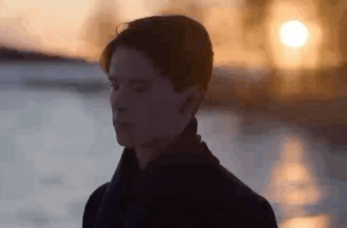 a young man is standing in front of a body of water .