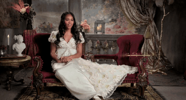 a woman in a long white dress sits on a red couch