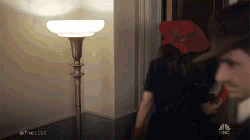 a man and a woman are standing next to each other in a room . the woman is wearing a red hat .