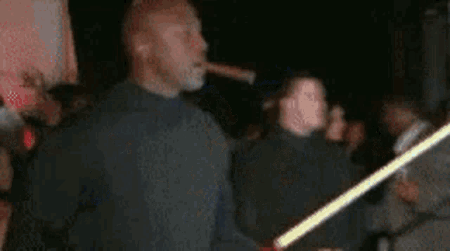 a man is smoking a cigar and holding a light saber in a crowded room .