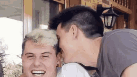 two men are laughing together and one of them is kissing the other 's forehead .