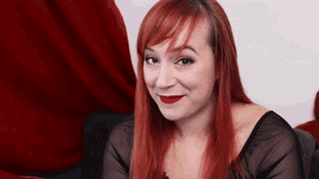 a woman with red hair is wearing red lipstick and a black top
