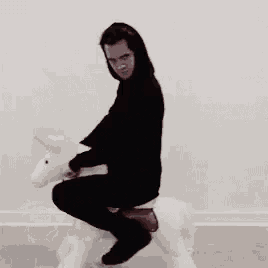 a man in a black hoodie is riding on the back of a rocking horse .