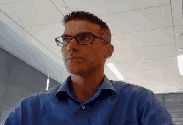 a man wearing glasses and a blue shirt looks serious