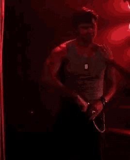 a man is dancing on a pole in a dark room with red lights behind him .