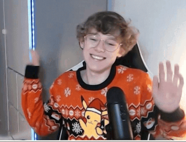 a young boy wearing a christmas sweater is sitting in front of a microphone and waving .