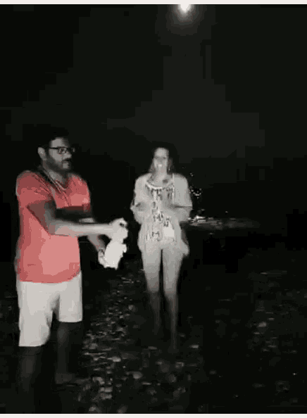 a man and a woman standing on a beach at night with a full moon in the background