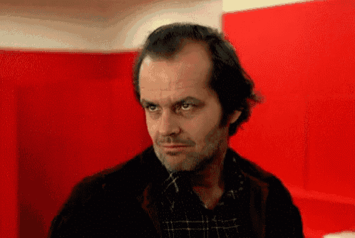 a man with a beard is standing in front of a red wall looking at the camera .