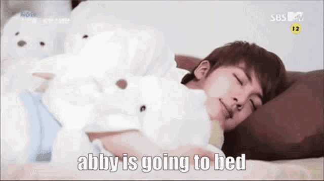 a man is laying in bed with a teddy bear and the words abby is going to bed above him .