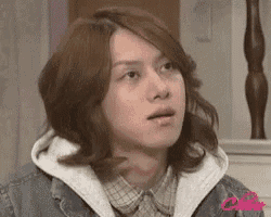 a young man with long hair is wearing a plaid shirt and a denim jacket .