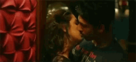 a man and a woman are kissing in front of a red wall .