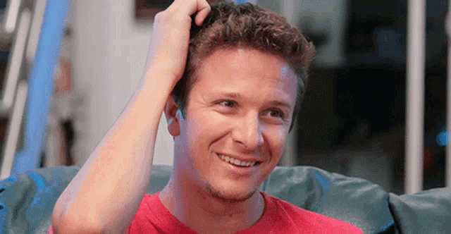 a man in a red shirt is scratching his head and smiling