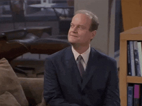 a man in a suit and tie is sitting on a couch in front of a bookshelf with the word pro on it .