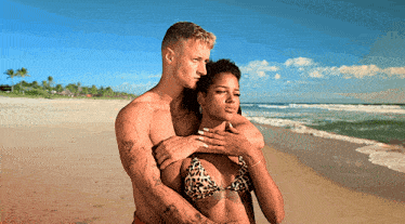 a man and a woman hugging on the beach with the man 's arm around the woman 's shoulder