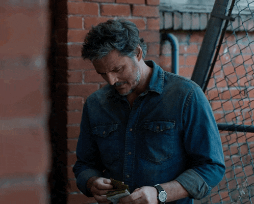 a man in a denim shirt is holding a stack of money in his hands