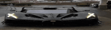 a black sports car is parked in a parking lot with the headlights on .