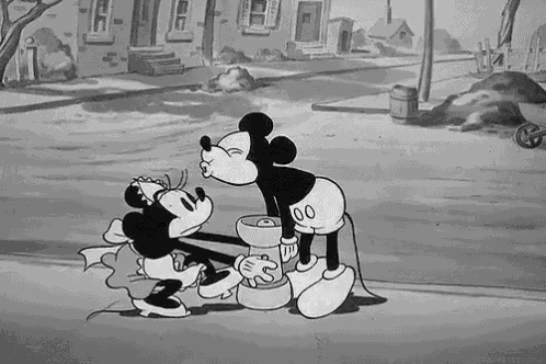 mickey mouse is kissing minnie mouse on the cheek in a black and white cartoon .