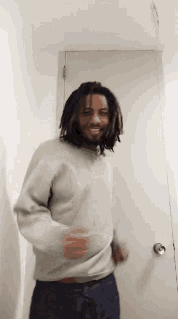a man with dreadlocks is standing in front of a white door .