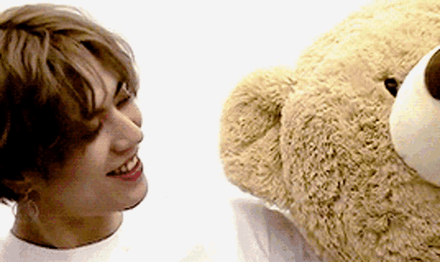 a young man is smiling next to a large teddy bear ..