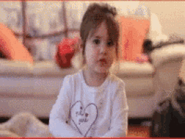 a little girl with a heart on her shirt is sitting on the floor