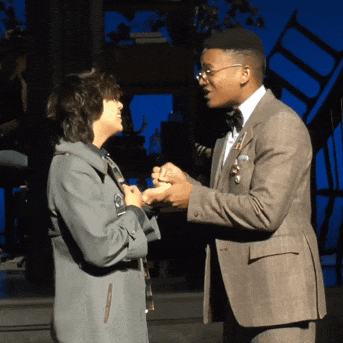 a man in a suit and bow tie holds hands with a woman