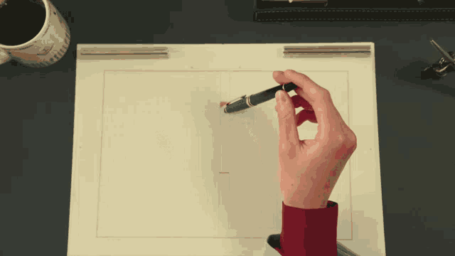 a person holding a pen on a piece of paper with a cup of coffee in the background