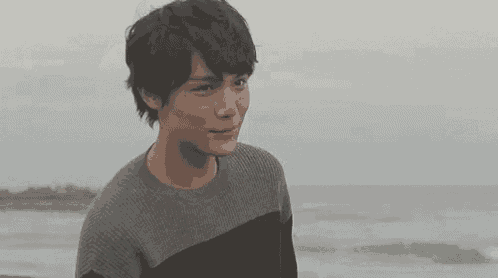 a young man is standing on a beach wearing a sweater and smiling at the camera .