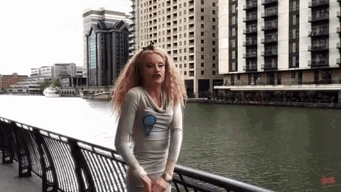 a woman is standing on a railing overlooking a body of water with buildings in the background