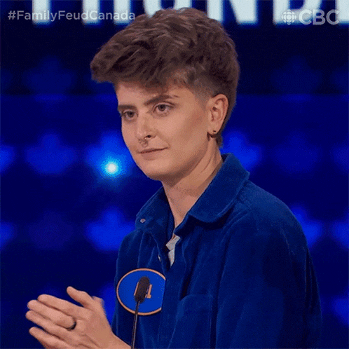 a young woman in a blue shirt is clapping her hands while standing in front of a microphone .