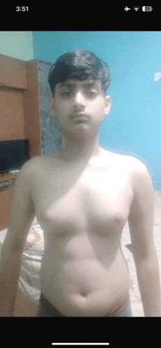 a shirtless boy is standing in front of a blue wall with the time of 3:51 on his phone