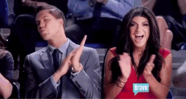 a man and a woman are sitting in a stadium clapping their hands together .