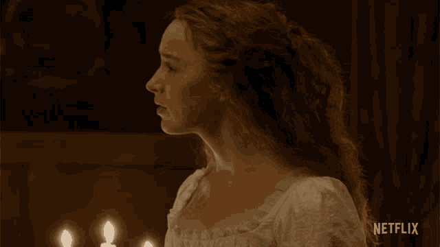 a woman in a white dress is standing in front of a candle with a netflix logo behind her