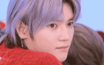 a close up of a person with purple hair wearing a red sweater and earrings .