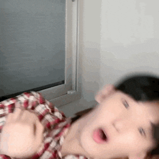a man in a plaid shirt is sitting in front of a window and making a funny face .